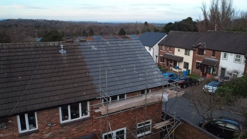 A brick residential building with a partially replaced dark roof, featuring scaffolding during a renovation process.