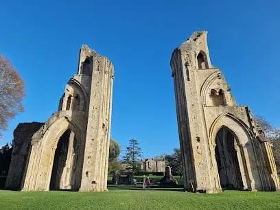 Ruined stone arches of Glastonbury Abbey, with clear blue sky and green grass.