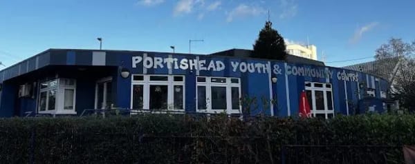 Portishead Youth & Community Centre, blue building with white lettering.  Windows, green hedge, and trees visible.