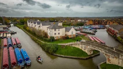 Canal scene with colorful boats, bridge, and buildings under a cloudy sky.