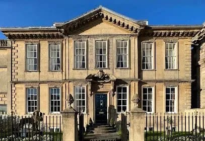 Georgian-style, two-story stone building with symmetrical windows and a central entrance. A fence is in the foreground.