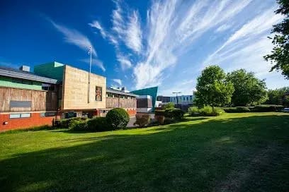 Building with green and brown exterior, grassy lawn, blue sky with wispy clouds.