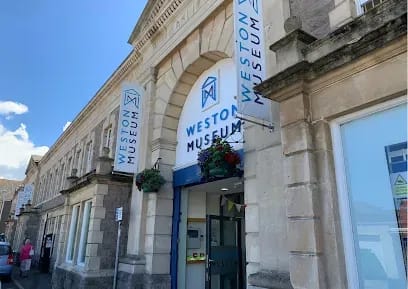 Weston Museum entrance with blue banners, cream stone facade, and hanging flowers.