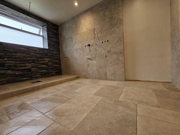 Bathroom interior with stone tiles on floor, window, and wall. Recessed lighting.