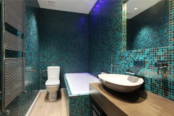 Modern bathroom with teal mosaic tile walls, white fixtures, and wood-tone counter and flooring.