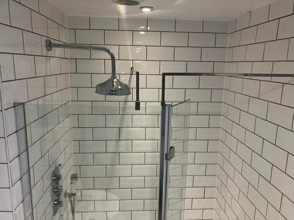 White-tiled shower stall with a rain shower head, chrome fixtures, and a glass door.