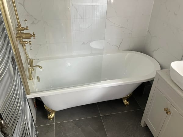 Claw-foot bathtub with gold fixtures, marble tile, and white vanity in a modern bathroom.