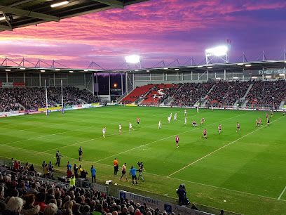 Rugby game in stadium under sunset sky; players on field, crowd in stands.