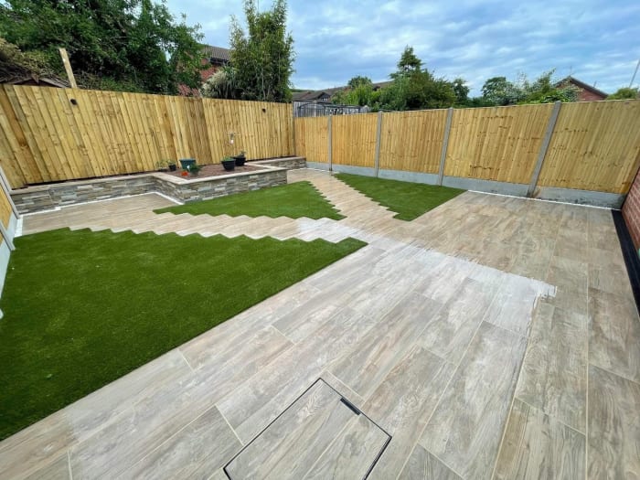 A backyard with green turf and stone patio, enclosed by a wooden fence.