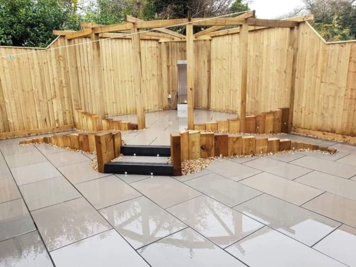 Wooden pergola and fence built on a stone patio; steps lead to interior space.