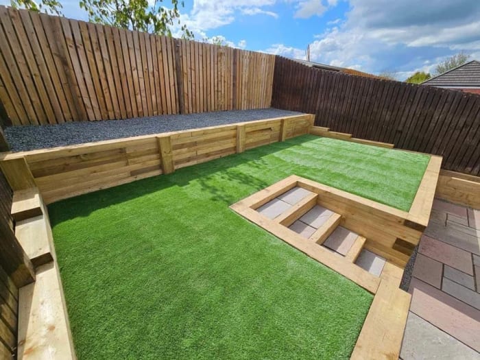 Raised garden bed with artificial grass, wooden steps, and a wooden fence.