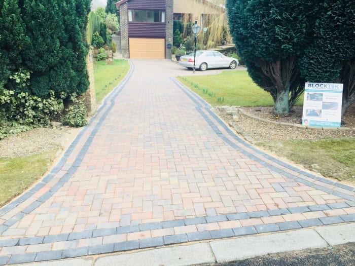 Brick paved driveway leading to a house with a car parked on the lawn.