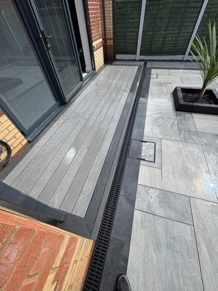 Outdoor patio with grey decking and stone pavers, a drain, and a potted plant.