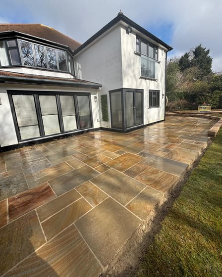 Indian sandstone patio laid across the rear of a detached house with bi-fold doors.