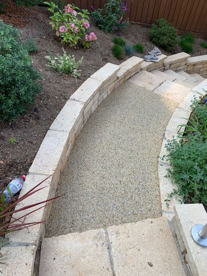 Curved resin-bound path bordered by natural stone walls and planted flower beds.