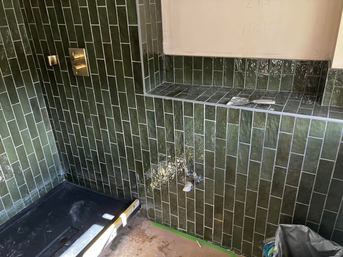 Green tiled shower with gold fixtures and pink wall, under construction.
