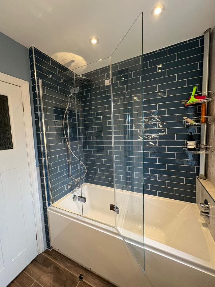 A bathroom with a bathtub, glass shower screen, and blue tiled walls.