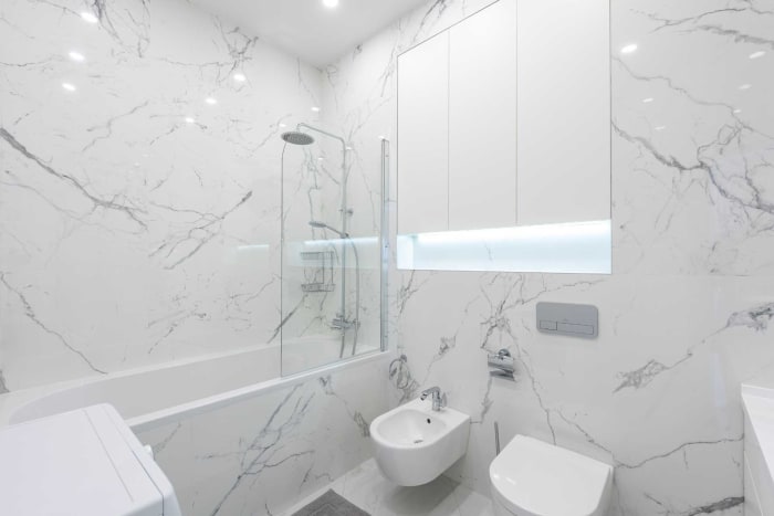 White marble bathroom with tub, shower, toilet, bidet, and storage cabinet.