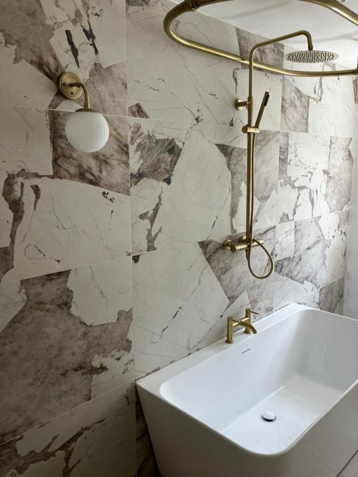 White bathtub, gold fixtures, marble tile wall, and a globe light in a bathroom.