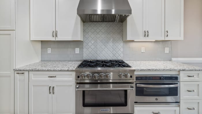 Stainless steel stove and oven in a white kitchen with granite countertops and white cabinets.