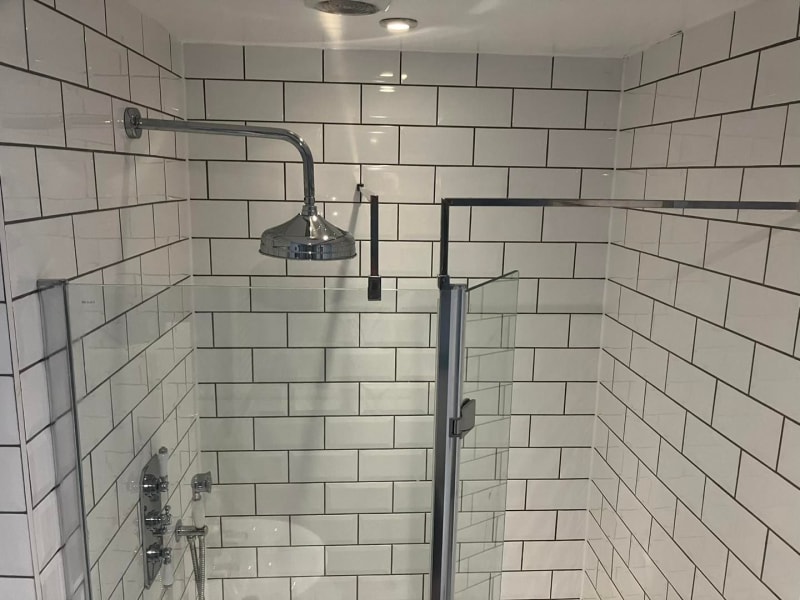 White tiled shower stall with glass door and chrome fixtures.
