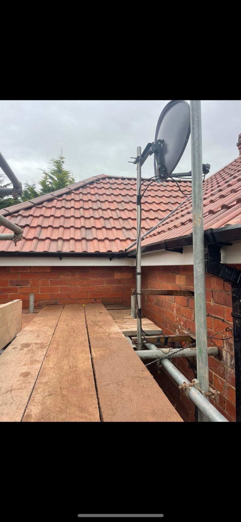 A large circular saw blade attached to metal scaffolding on the side of a brick house with a tiled roof.