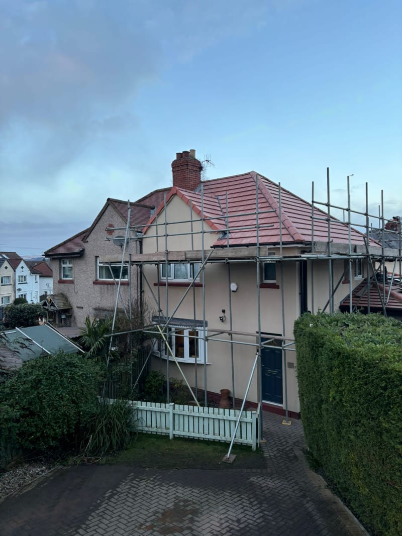 A detached house under renovation with scaffolding around the front facade and a newly tiled roof.