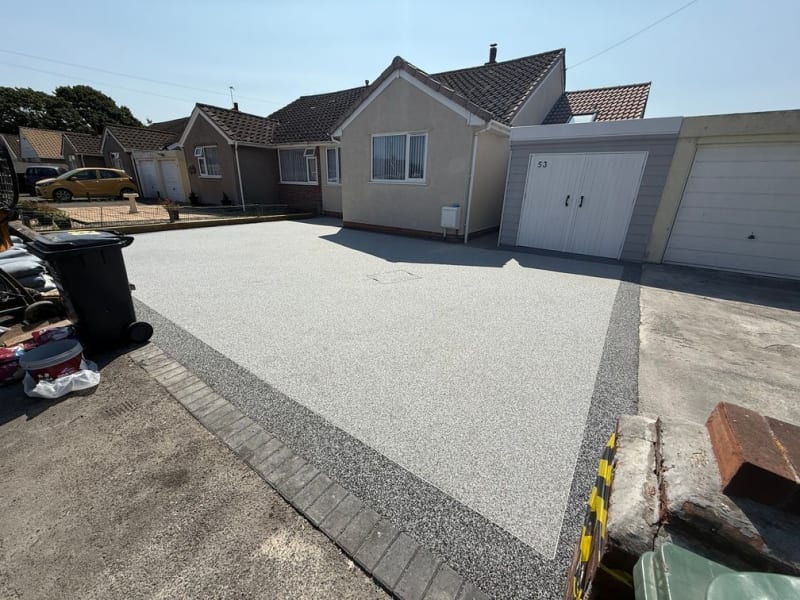 Dark grey resin driveway in front of black garage door, with block paving border