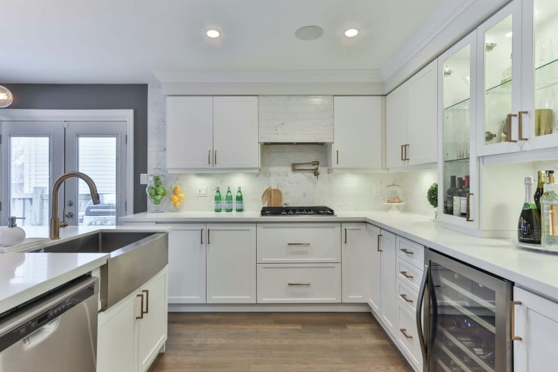 Modern white kitchen with stainless steel appliances, a wine fridge, and wooden floor.