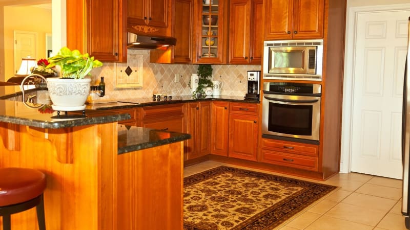 Kitchen with wooden cabinets, granite countertops, and a floral rug.