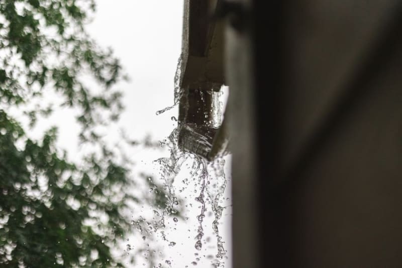 Water pouring off the edge of a roof past a blocked gutter in Croydon