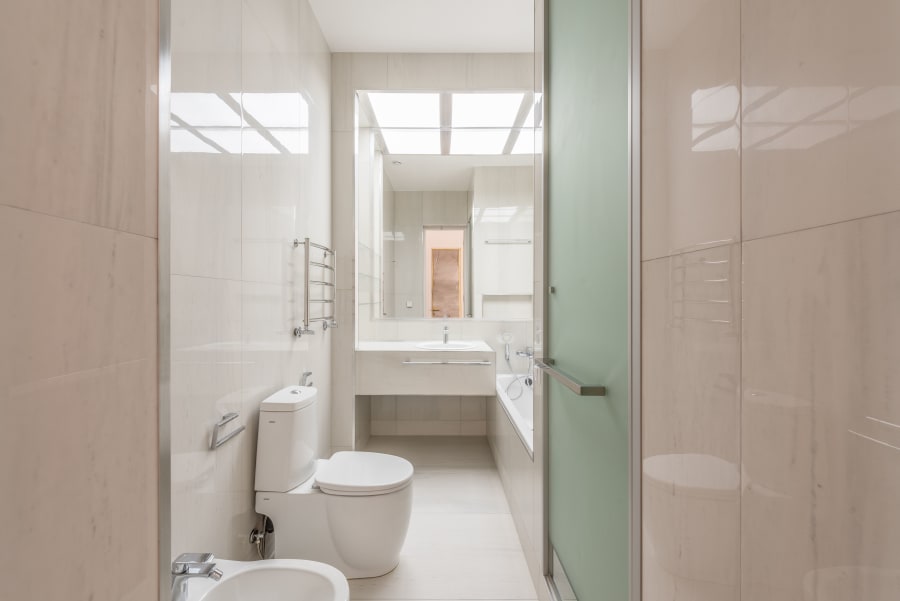 Bright tiled bathroom with toilet, sink, shower, and frosted glass door.
