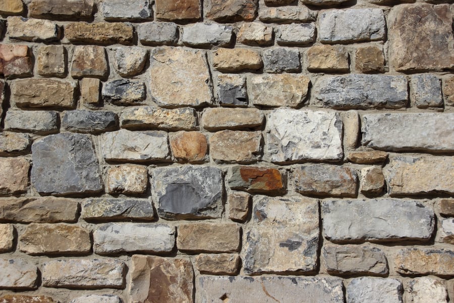 Rough stone wall with irregular tan, gray, and brown bricks and mortar lines