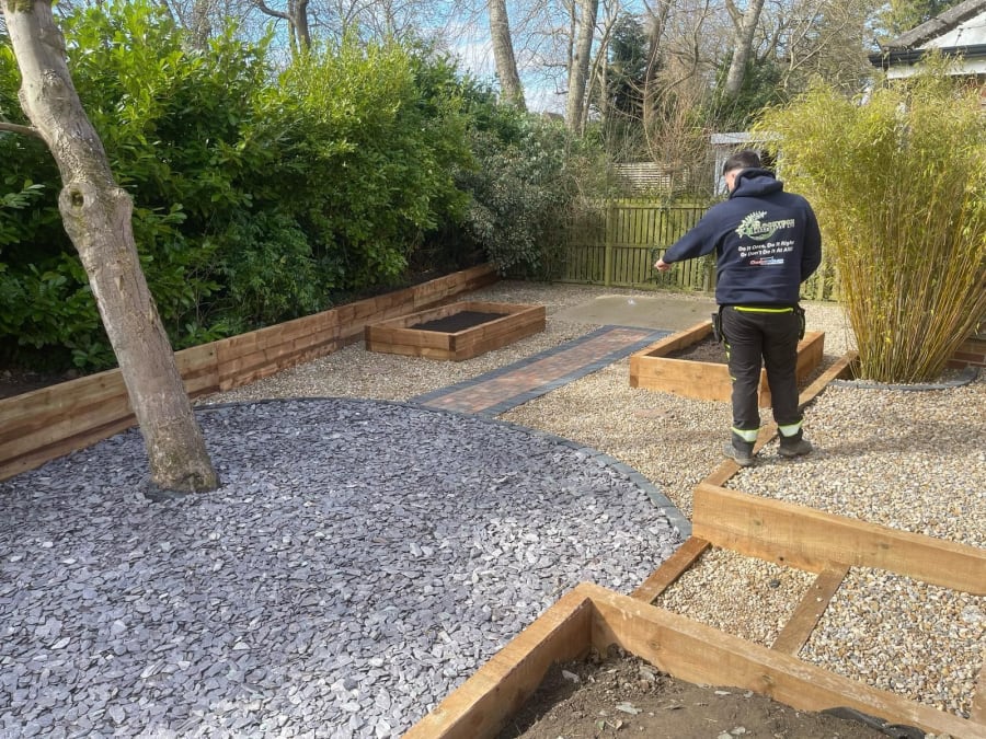 Worker installing gravel in a landscaped garden path with timber edging and bushes nearby