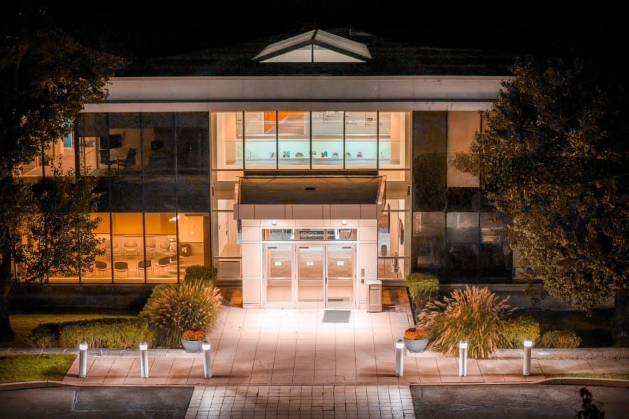 Lit modern building entrance at night with glass doors and glowing windows