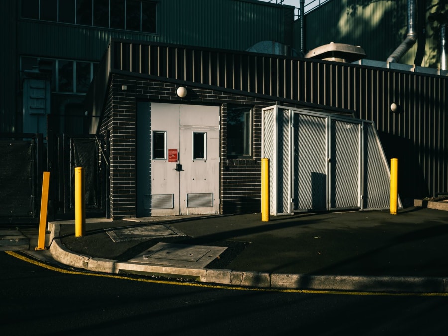 Industrial building entrance with white doors, yellow bollards, and a curved curb at night