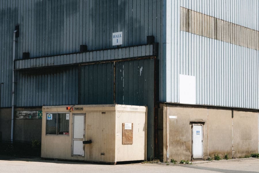 Industrial warehouse exterior with a small beige portable office trailer in front of a large metal door