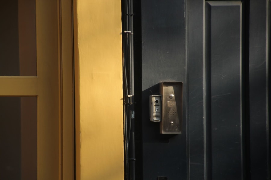 Wall-mounted doorbell intercom on a dark door beside a yellow wall.