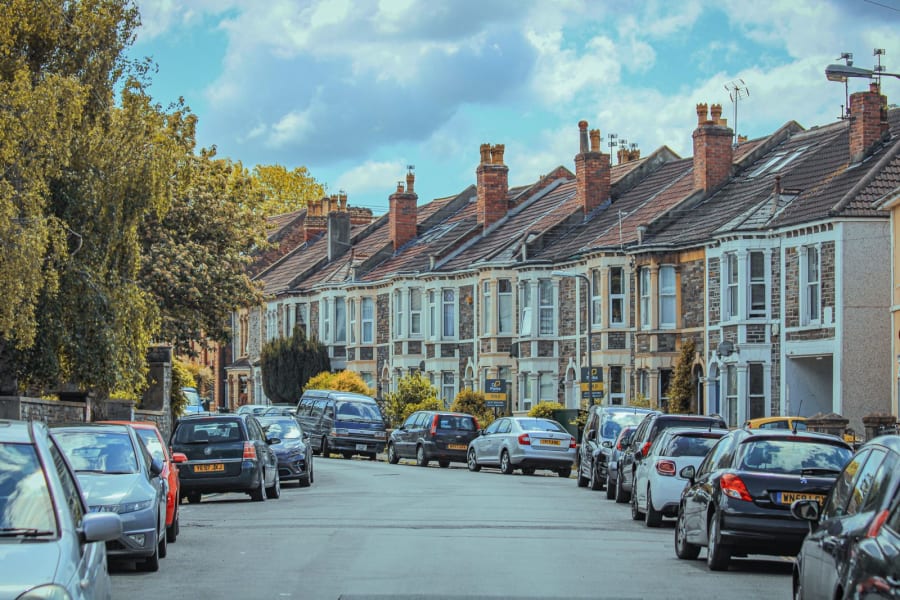 Quiet residential street with parked cars and row houses under a blue sky