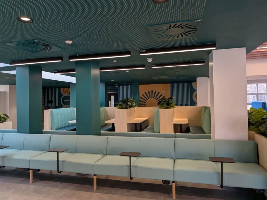 Modern lounge with teal seating, light wood tables, and a sunburst wall feature