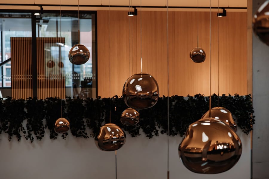 Modern lobby with hanging copper sphere lights and dark greenery against wood-paneled walls