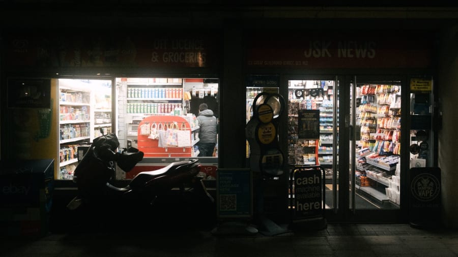 Nighttime street scene with a person on a scooter beside a brightly lit convenience store