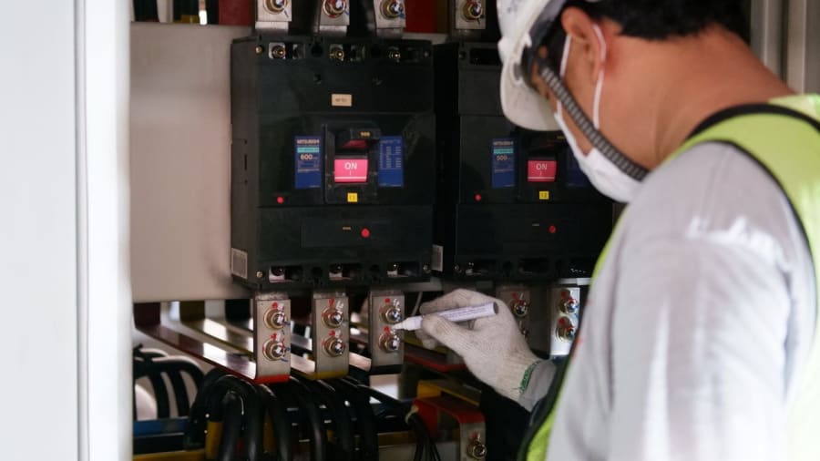 Technician inspecting electrical control panel with gloves and mask inside a cabinet
