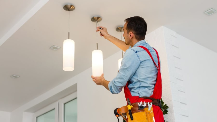 Technician installing two pendant lights on a white ceiling with a tool
