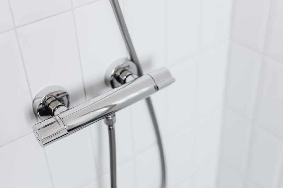 Chrome shower faucet and handheld showerhead on white tiled bathroom wall