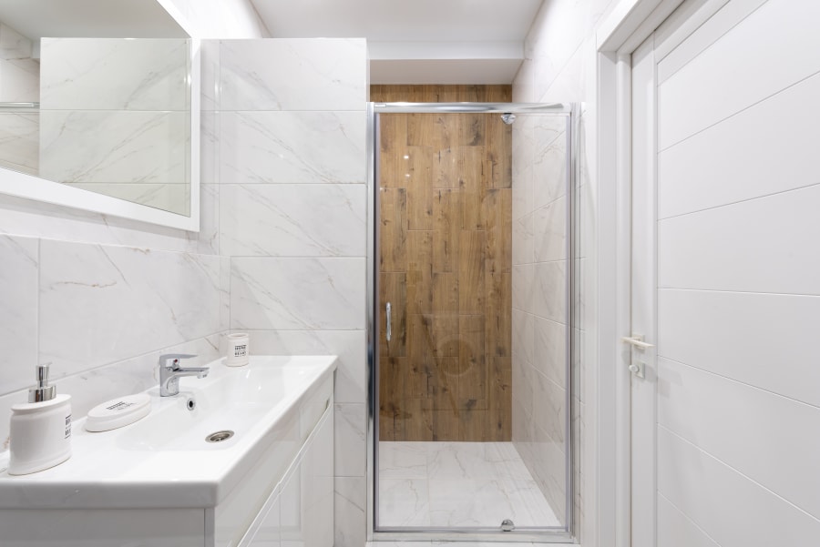 Modern white bathroom with vanity, mirror, tiled shower, and wood-look shower door