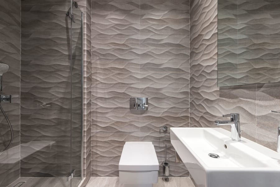 Modern bathroom with textured gray tile, wall-mounted toilet, and white sink vanity