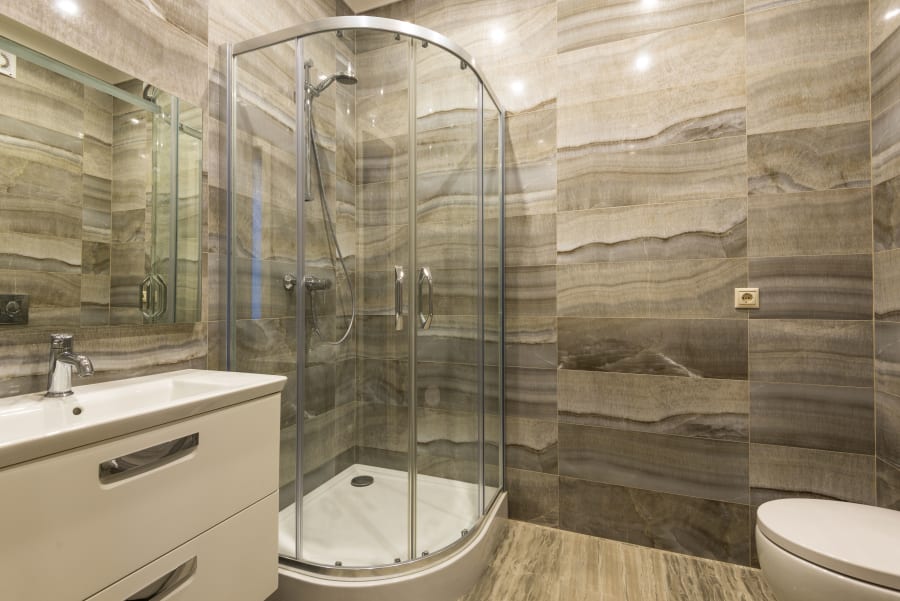 Modern bathroom with glass shower, white vanity, and beige stone tile walls