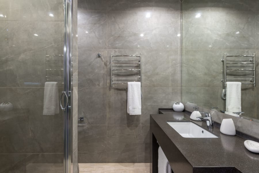 Modern bathroom with gray tiled walls, glass shower, and dark vanity with sink and towel rack.