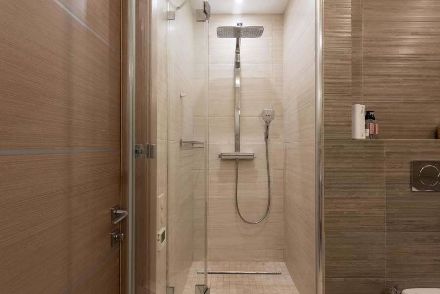Small tiled bathroom shower with glass doors, chrome rainfall showerhead, and a hand-held shower sprayer.